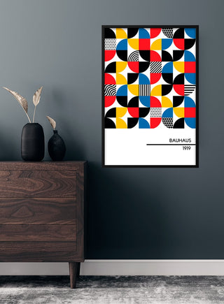 1919 Bauhaus Poster #5 with colorful geometric shapes, framed and displayed on a dark wall above a wooden dresser.