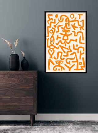 Paul Klee orange art poster with abstract figures in a black frame, hanging on a dark wall above a wooden dresser.