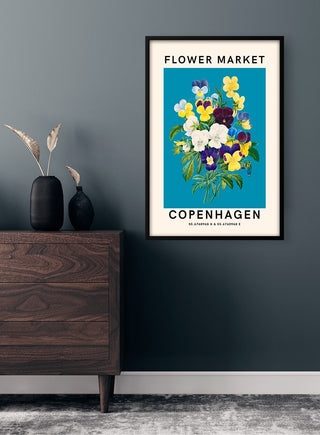 Poster of colorful flowers labeled "Flower Market Copenhagen" hanging on a dark gray wall above a wooden dresser.
