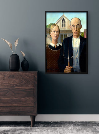 Framed "American Gothic" poster by Grant Wood displayed on a dark wall above a modern dresser.