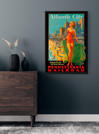 Framed vintage Atlantic City poster on a grey wall above a wooden dresser with decorative vases.