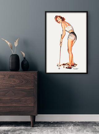Framed vintage golf advertising poster featuring a woman golfer, displayed above a wooden dresser in a modern room.