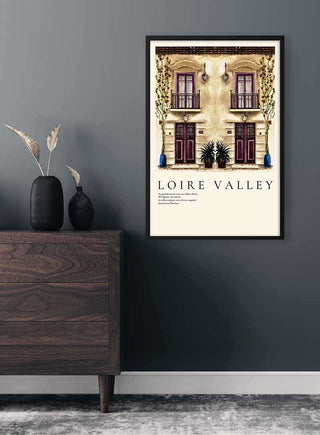 Framed poster of an Old French townhouse in the Loire Valley hanging on a dark gray wall above a wooden dresser.
