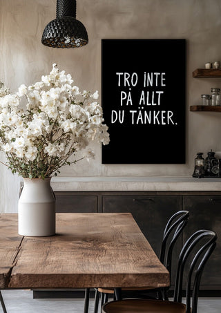Tro inte på allt du tänker by Grafik bageri in a black frame above a rustic table with white flowers