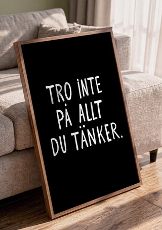 Tro inte på allt du tänker by Grafik bageri in a walnut frame leaning against a grey sofa