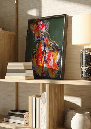Red Figure by René J in a dark frame on a wooden shelf beside books and a lamp