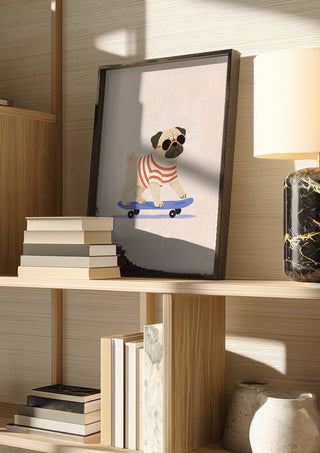 Pug on a Skateboard by Decker Studios in a dark frame on a wooden shelf beside books and a lamp
