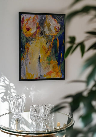 Torso in Yellow by René J in a black frame above a glass table with crystal glassware