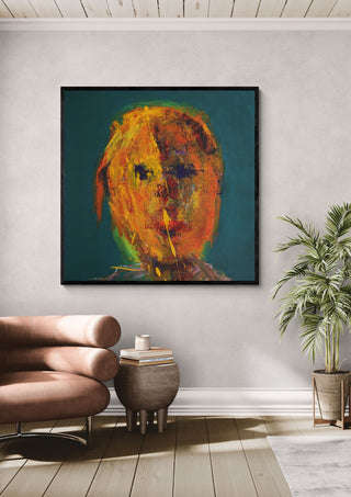 Head in Orange by René J in a black frame above a tan leather chair beside a potted plant