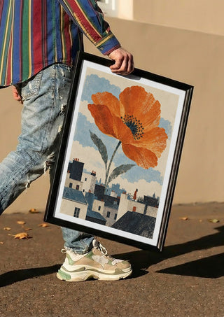 Blooming Above the Roofs by Matthews Gallerie carried in a black frame along a sunny street