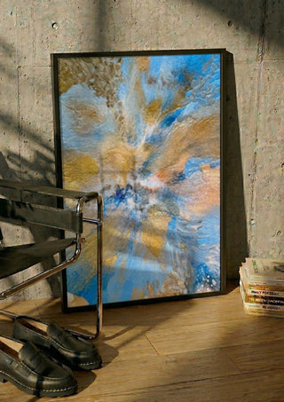 Sand and Sky by Da Winters in a black frame leaning against a concrete wall by a steel chair