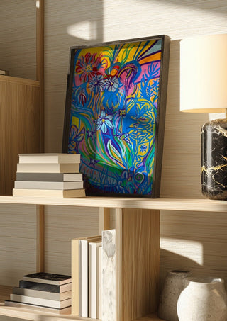 Garden Party by Da Winters in a dark frame on a wooden shelf beside books and a lamp