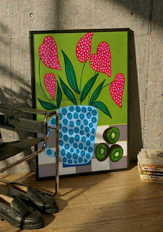 Kiwi My Heart by LGDyrby in a black frame leaning against a concrete wall by a steel chair