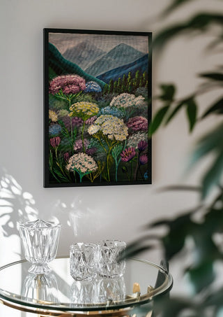 Mountain Meadow by Svetla Stoyanova Bassi in a black frame above a glass table with crystal glassware