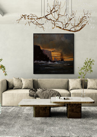 Ship by the Cliffs by Justyna Kopania in a black frame above a cream sofa under a branch chandelier