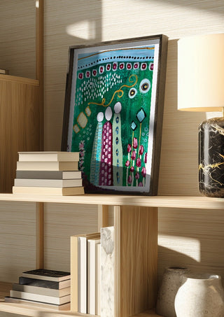 Fairy Tale 2 by Art Anne Lee in a dark frame on a wooden shelf beside books and a lamp