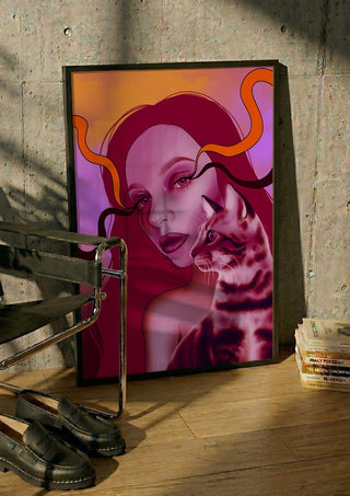 Glow And Purr by Sabrina Rosenblatt in a black frame leaning against a concrete wall by a steel chair