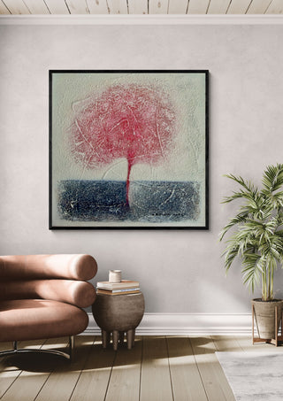 Red Tree by Marina Agre in a black frame on a pale wall above a tan leather chair and a potted palm