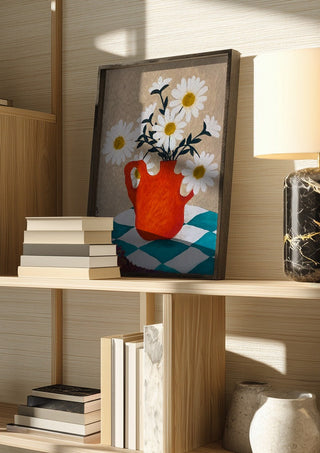 Vita blomster i röd vas by Rebecka Hansson in a dark frame on a wooden shelf beside books and a lamp