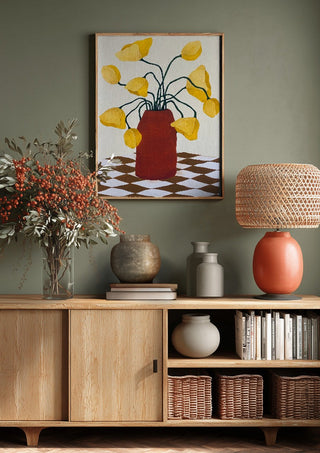 Gula blomster i terracottafärgad vas by Rebecka Hansson above a wooden sideboard on a sage green wall