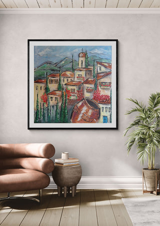 Cyprus village by Dina in a black frame above a pink armchair beside a palm