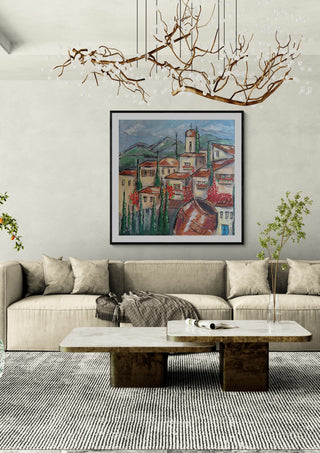 Cyprus village by Dina in a black frame above a beige sofa under a branch chandelier