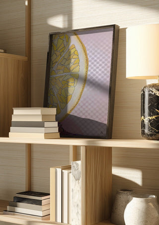 Lemon Slice by L.OE. Art in a dark frame on a wooden shelf beside books and a lamp