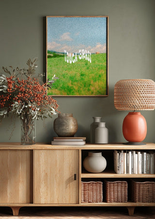 Touch Grass by Jakob Falkenberg above a wooden sideboard on a sage green wall