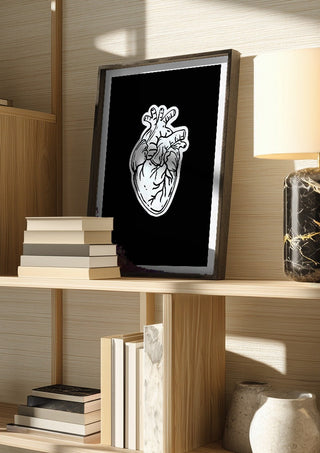 Still Beating by Nari in a dark frame on a wooden shelf beside books and a lamp