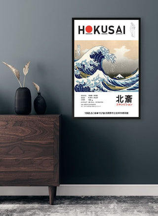 Framed print of Hokusai's The Great Wave displayed on a dark wall above a wooden cabinet with vases.