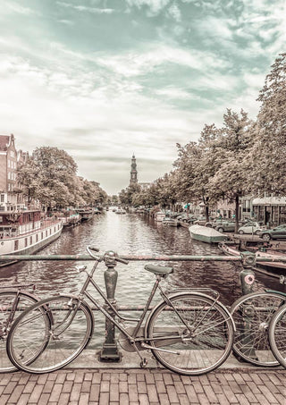 Two vintage bicycles on a bridge over an Amsterdam canal, urban vintage style with cityscape in the background.