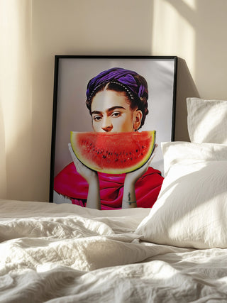 Framed artwork of a woman holding a watermelon slice, displayed on a bed in sunlight.