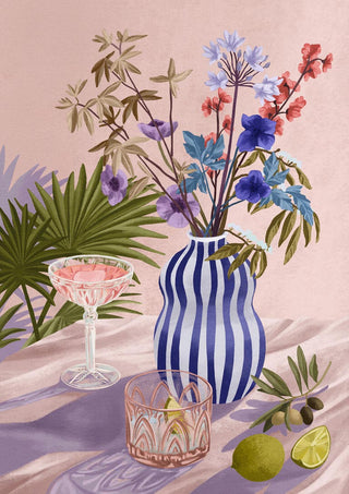 Striped blue vase with lilac and blue flowers, cocktail glass, lime, olives, and palm leaves on a pink background.
