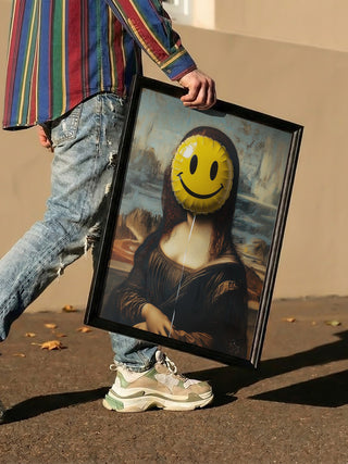 Person holding a framed parody of the Mona Lisa with a yellow smiley face over her head, outdoors.