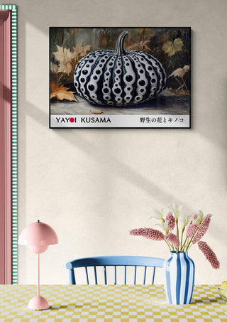 Framed Yayoi Kusama Black Pumpkin artwork on wall above table with pink lamp and vase of flowers.