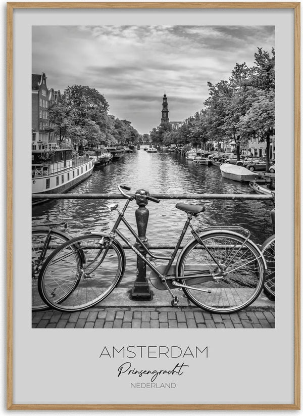 Black and white photo of a bicycle on a bridge over Amsterdam's Prinsengracht canal with boats and trees.