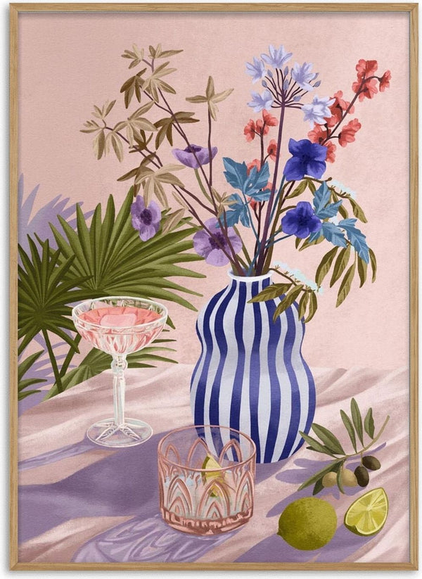 Striped blue vase with lilac and blue flowers, cocktail glass, lime, olives, and palm leaves on a pink background.