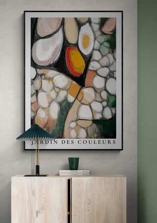 Abstract art poster "Jardin Des Couleurs" displayed above a light wooden cabinet with decor items.